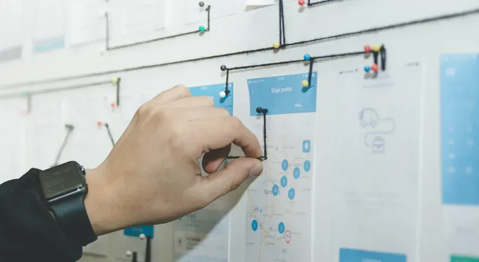 A hand using string and push pins to connect pages of a paper prototype