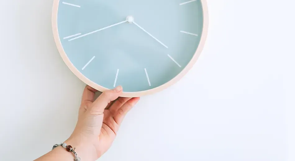 A hand holding an analogue clock up against a wall